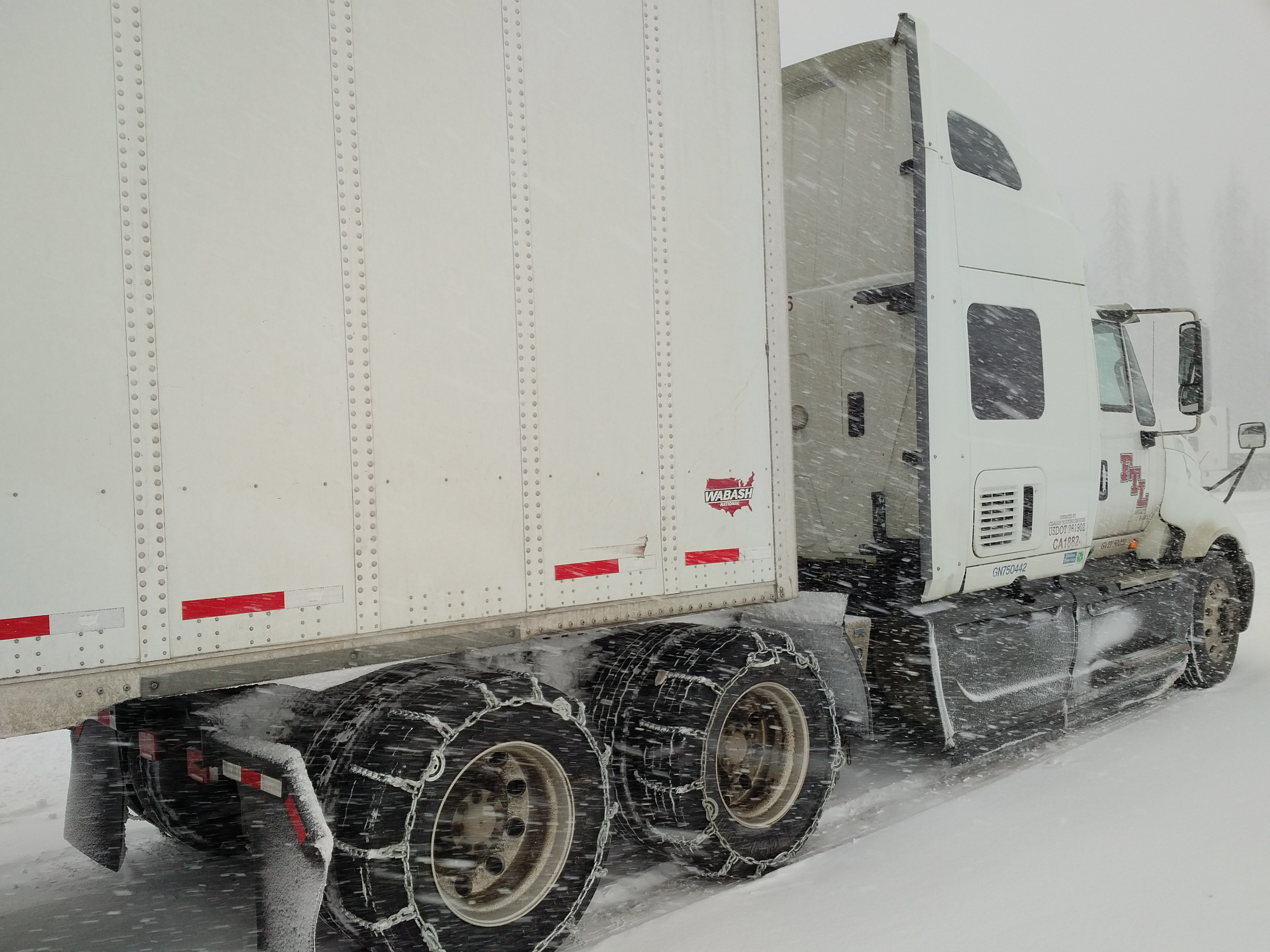 One semi-truck towing a trailer during a snowstorm.